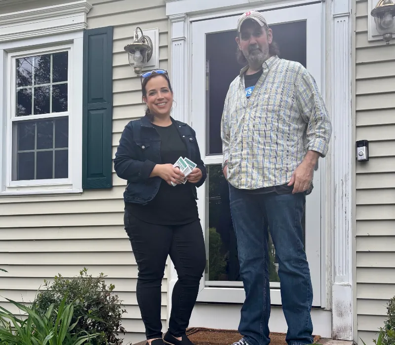 Suzy canvassing with a resident on the porch of a tan house