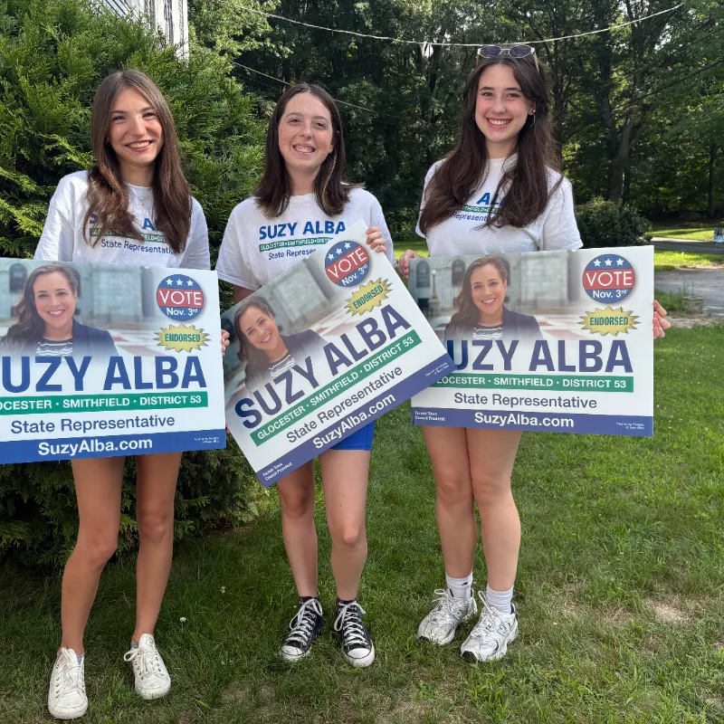 Three young volunteers holding Suzy Alba yard signs