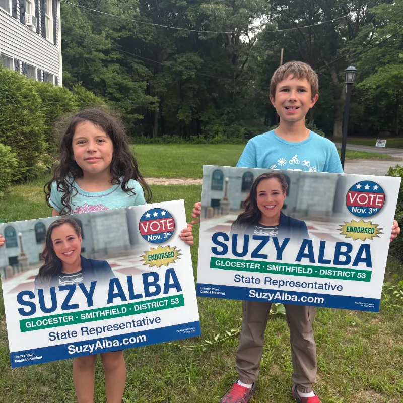 Two young volunteers holding Suzy Alba yard signs on a lawn