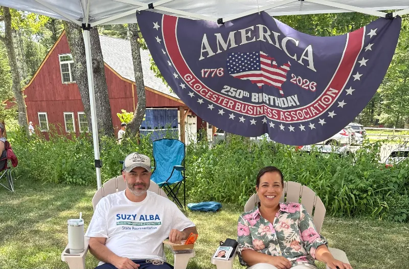Suzy and a supporter relaxing in lawn chairs under an America 250th birthday banner