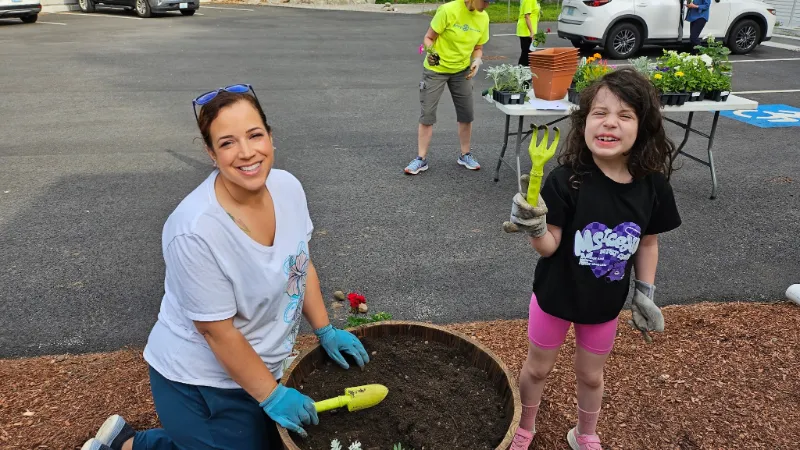 Suzy planting flowers with a young volunteer in a parking lot planter