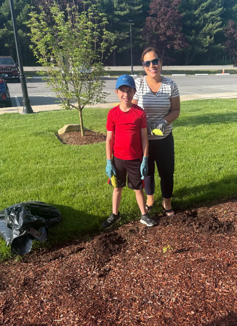 Suzy and a young volunteer planting a tree on a lawn